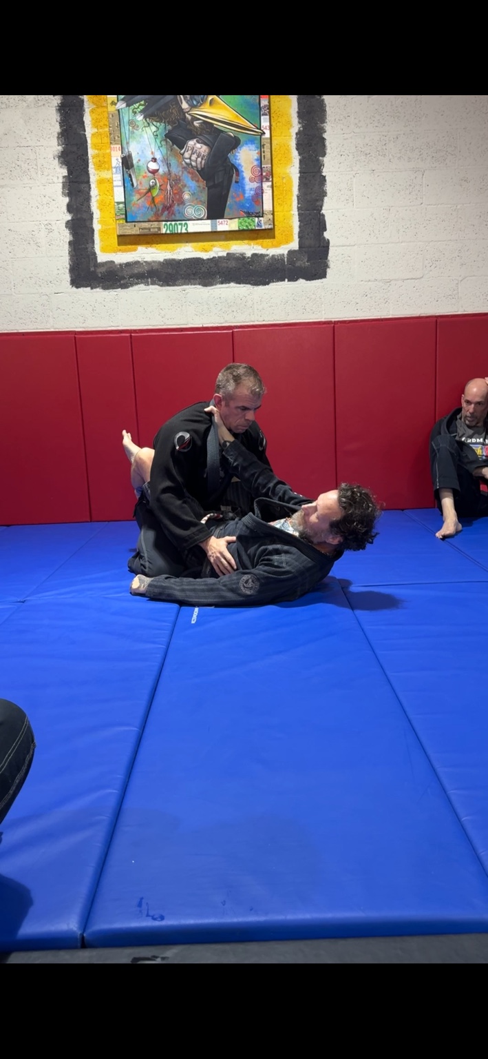 John demonstrating gi Jiu-Jitsu with a partner as a student watches
